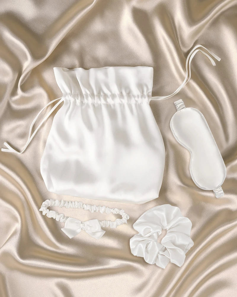 Set of white silk wedding gifts including a pouch, eye mask, silk bridal garter with bow, and scrunchie.